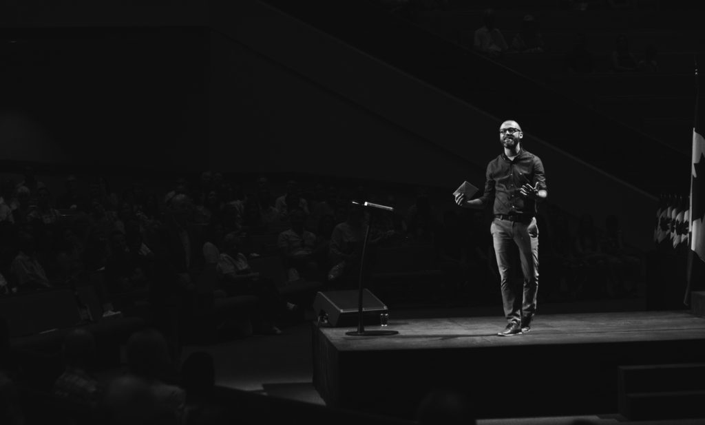 Image of a well-dressed man on a stage presenting to a crowd to show live poetry readings expectations