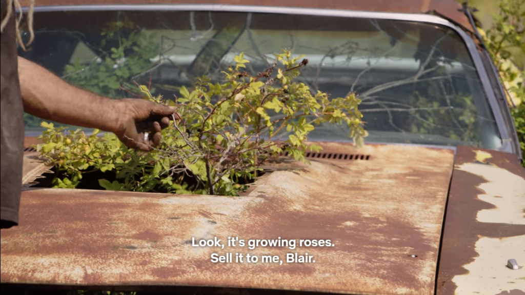 Screenshot of Mike Hall touching a rose growing from a Rust Valley Restorers classic car.