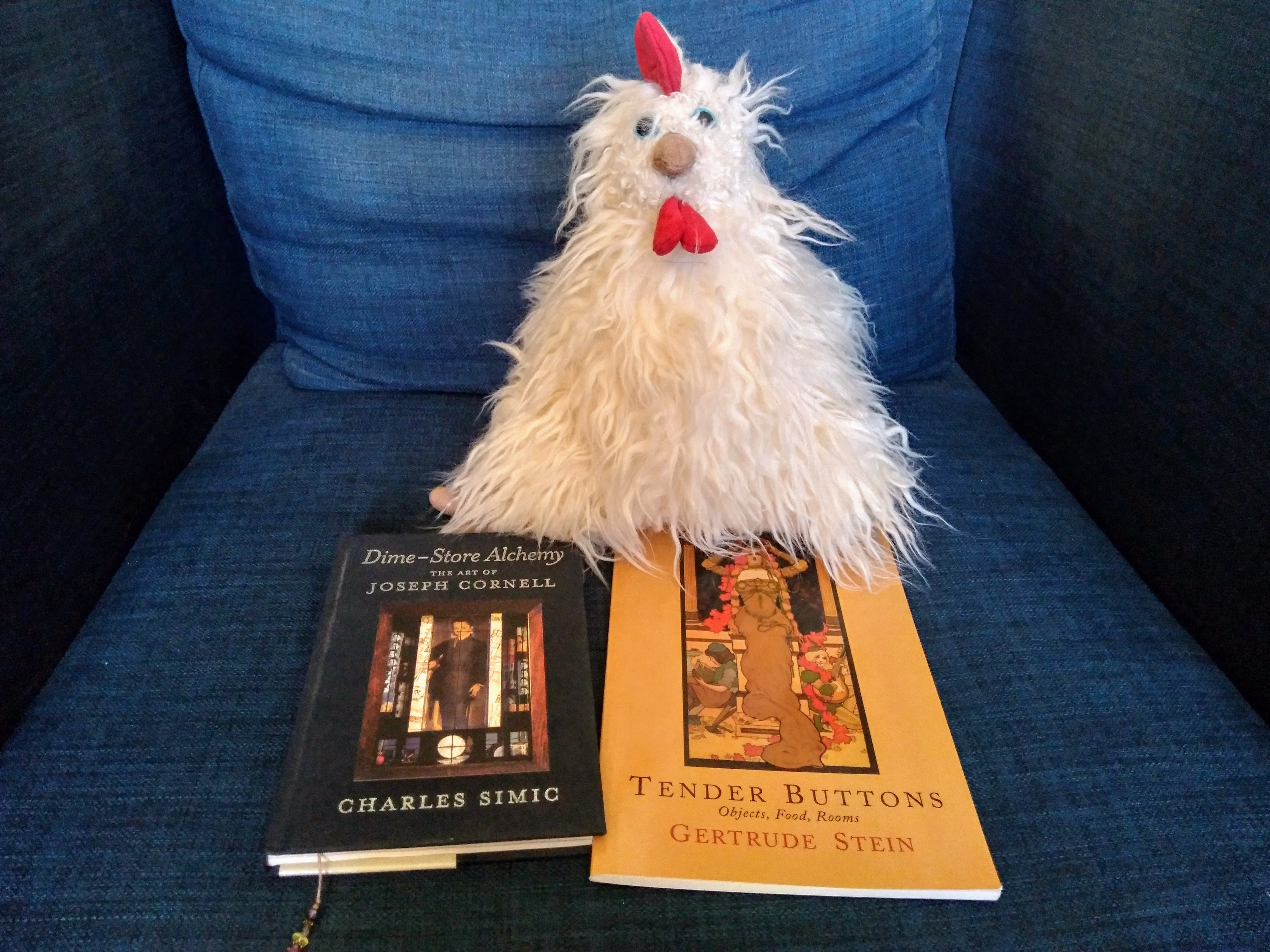 Prose poetry books and a chicken stuffed animal arranged on a couch